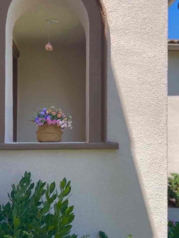 Warm brown-toned entrance featuring an arch-shaped window decorated with a bohemian flower basket and a hanging disco ball, creating a cozy atmosphere