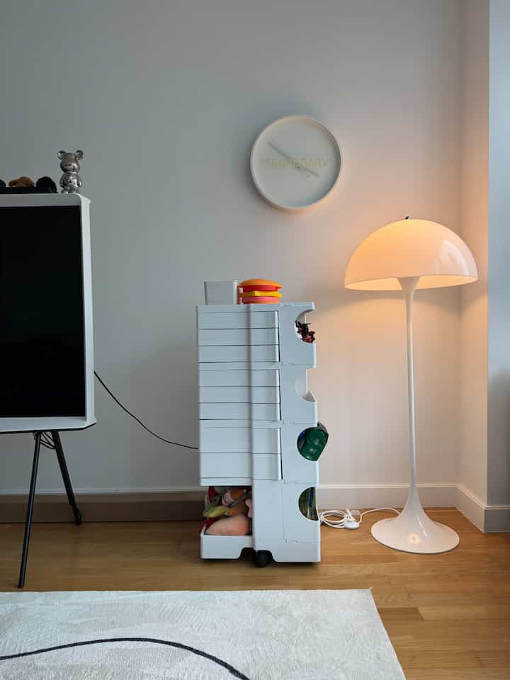 White-toned living room corner featuring functional Boby Storage Trolley, Panthella Floor Lamp, and a 'TEMPORARY' clock in a minimal modern setting