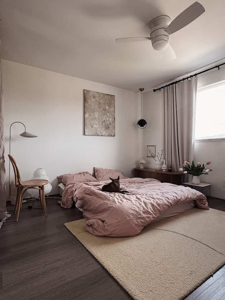 White and brown toned bedroom featuring pink bedding and a pet dog lying on the bed, creating a cozy atmosphere