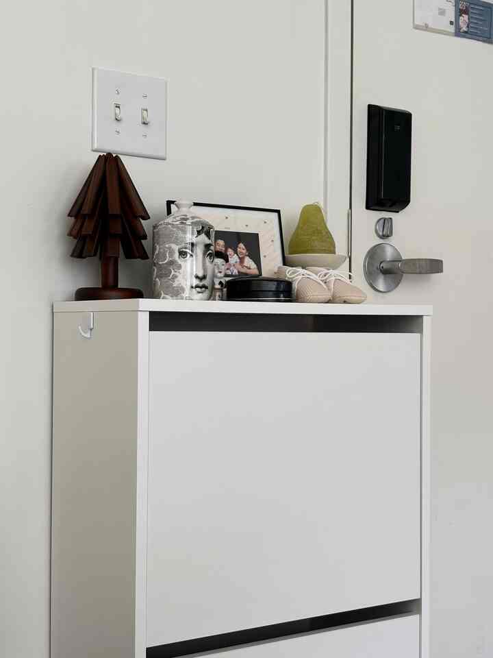 White-toned entrance with a clean shoe cabinet topped by wooden tree art and candles, creating a simple space