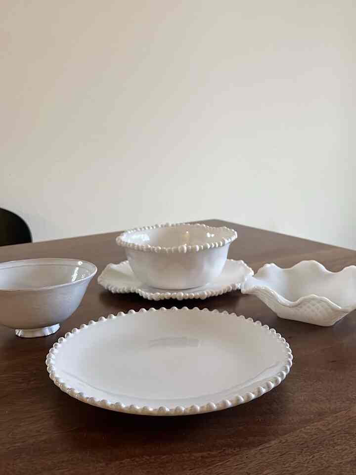 White-toned dining room featuring sleek Costa Nova white ceramic plates and bowls centrally placed on a wooden table in a natural modern style space