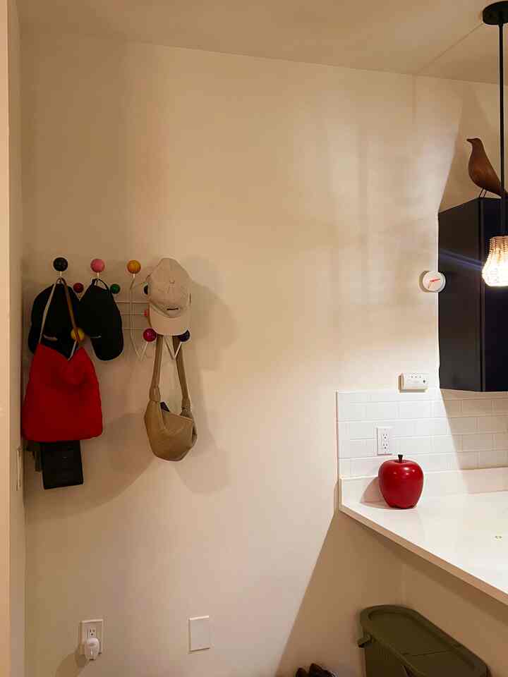 White and natural color toned entrance and part of kitchen space featuring wall-mounted storage and red accent decor in cozy atmosphere