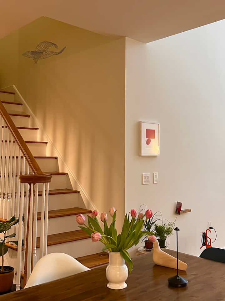 White walls and wood-tone dining table with stairs in a natural modern dining room featuring a vase with tulips at the center