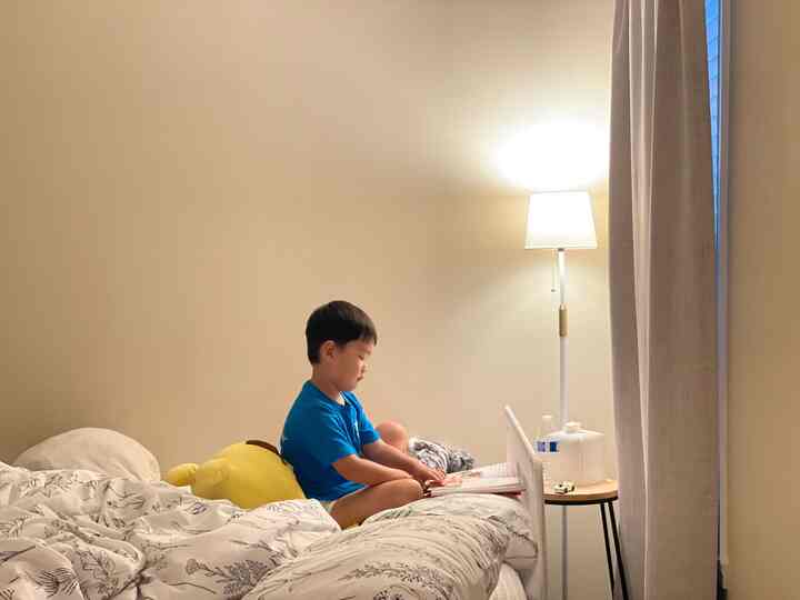 Beige-toned bedroom with a child sitting on the bed reading, featuring minimal and natural ambiance