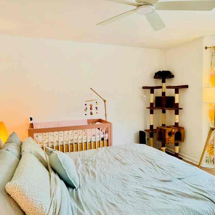 Bright white-walled bedroom with natural color furnishings, featuring a baby crib and cat tower in a simple layout