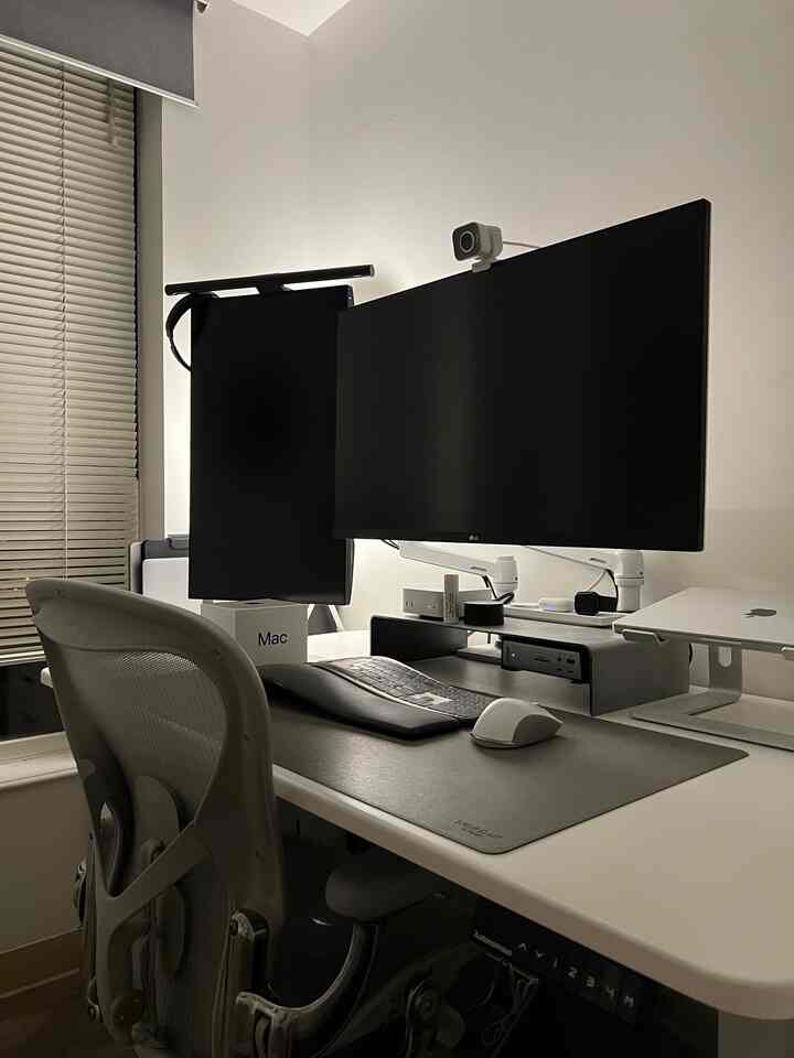 A white and gray tone home office featuring an Aeron chair and dual monitors arranged in a clean and modern workspace