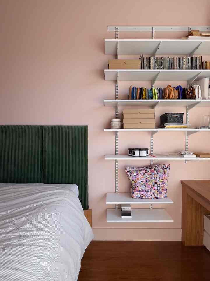 Bedroom with pink walls and green headboard, white bedding and tidy shelves create a natural, simple atmosphere