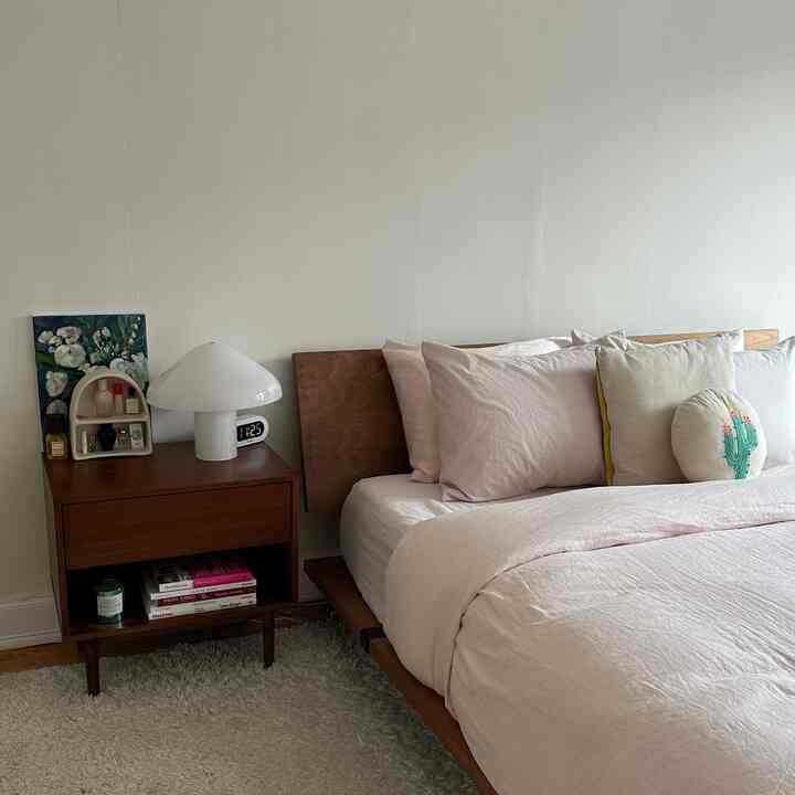 A cozy bedroom with soft natural colors, featuring a wooden bed and nightstand with a simple table lamp