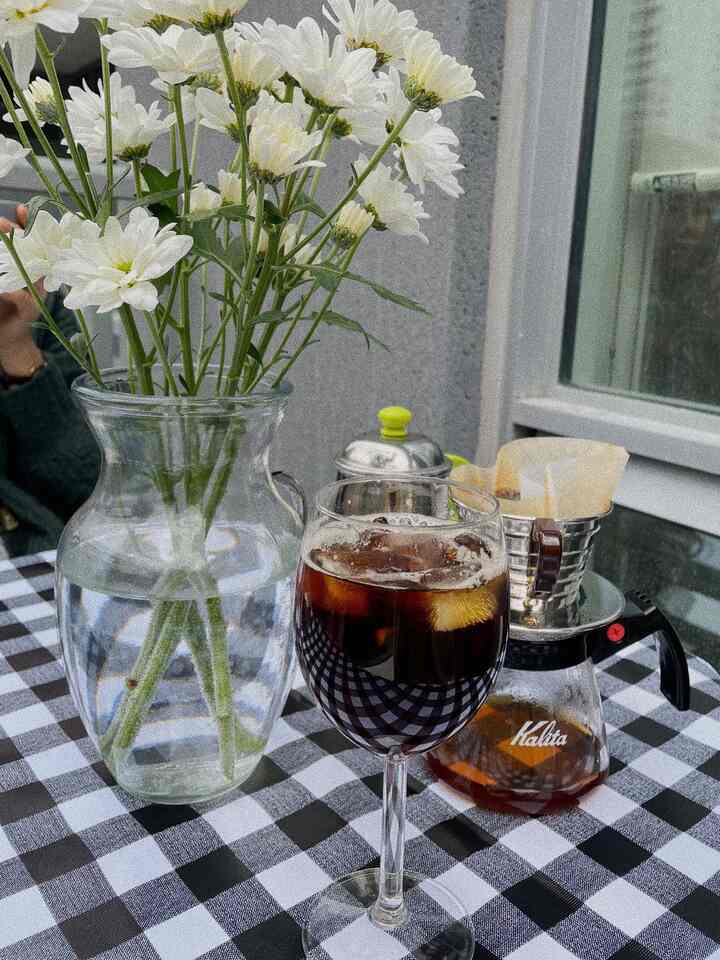Natural toned home cafe space with vase of white flowers and coffee drip set on black and white checkered tablecloth