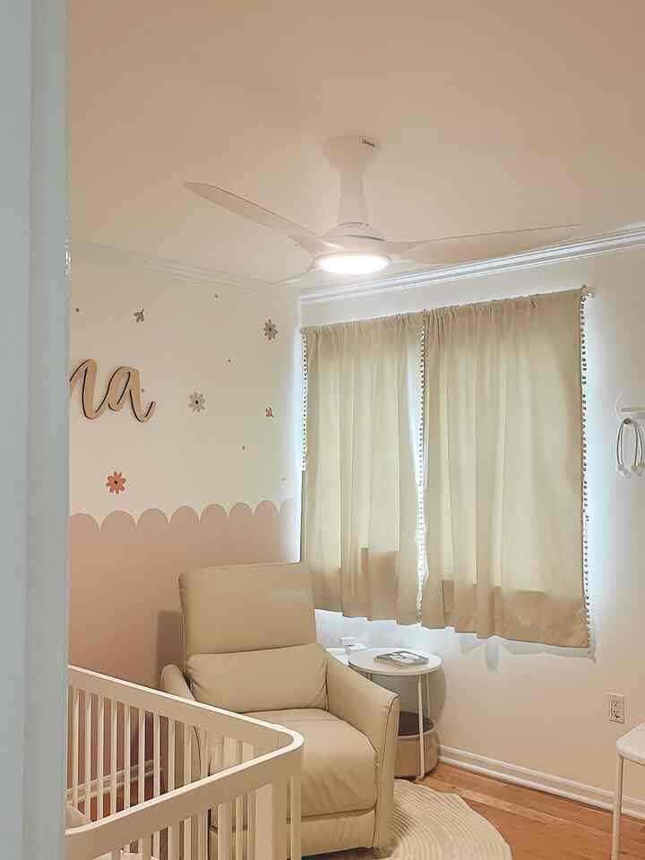 Natural toned kids' room featuring beige curtains, a central recliner with side table, and a crib in front creating a simple atmosphere