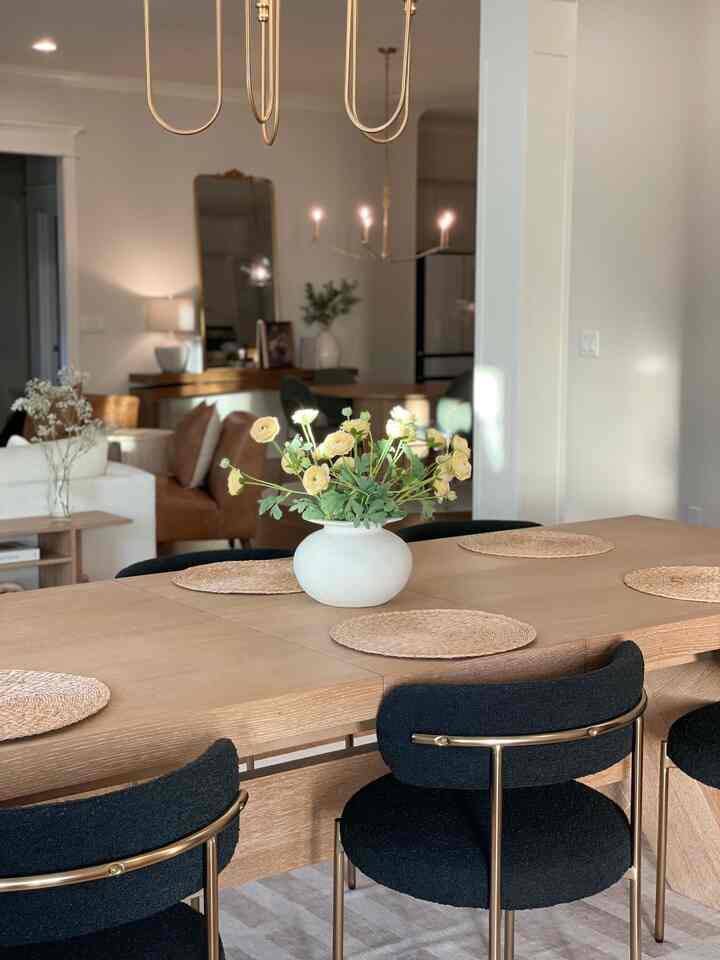 Natural wood tone dining room with modern furniture against white walls, featuring soft lighting and floral centerpiece, creating a cozy atmosphere