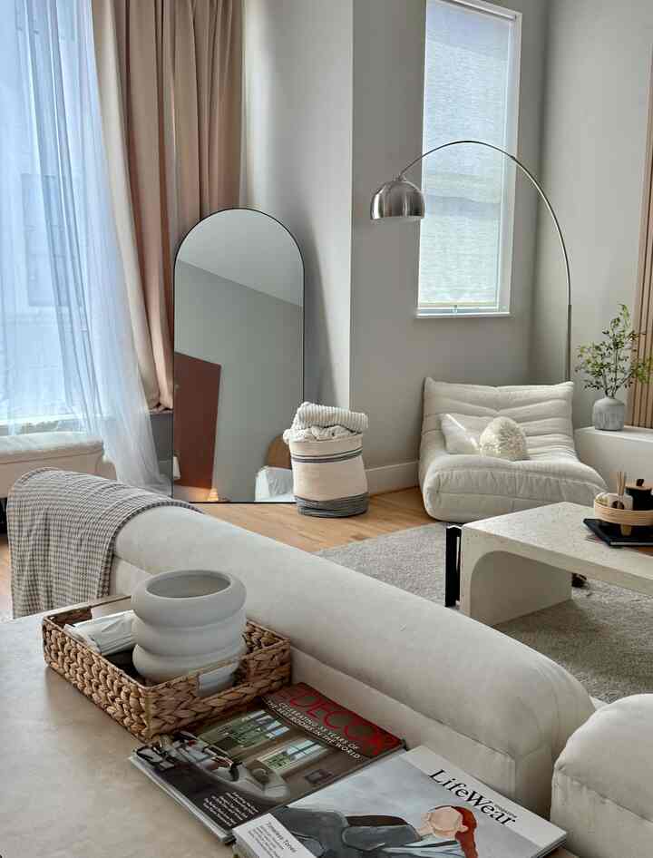 White and beige toned living room featuring sofa and arched floor lamp with a modern, soft ambiance