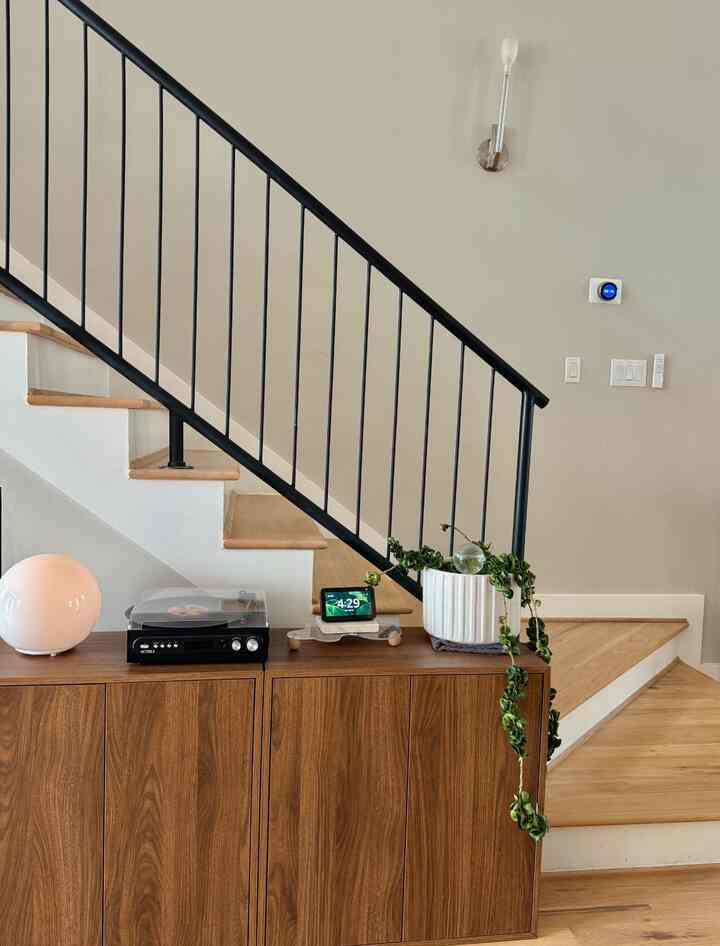 Wood tone and beige wall living room stair area featuring natural wood cabinets, floor lamp, and plants in a modern interior