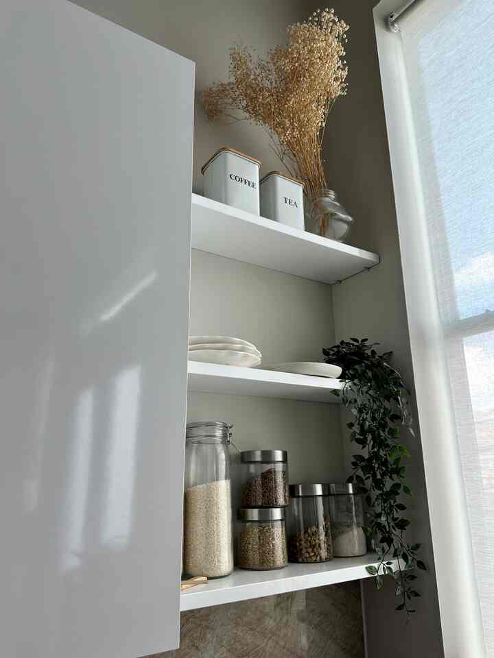 Natural-tone kitchen shelves featuring plates, storage jars, and a decorative plant with a stylish arrangement