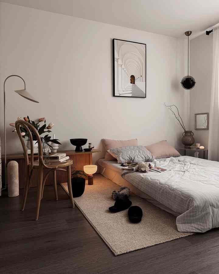 Beige and light brown toned bedroom with low bed, wooden chair, rug, and pendant light creating a cozy ambiance
