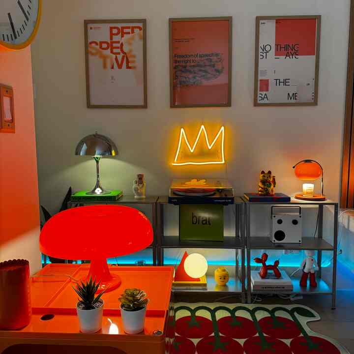 Vibrant red and orange-lit living room featuring neon crown sign and vintage posters on shelf setup
