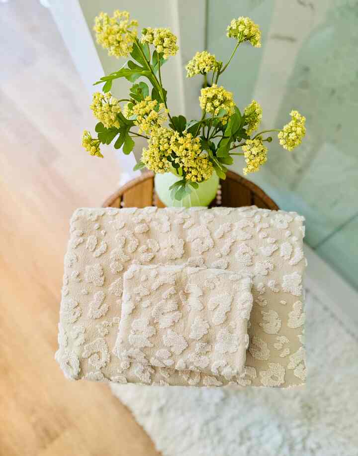 Natural-toned bathroom featuring beige leopard-patterned towels and yellow flowers on a wooden stand with a cozy atmosphere