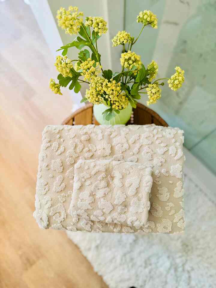 Natural color wooden table featuring beige towels and yellow flowers creating a cozy bathroom accessory space