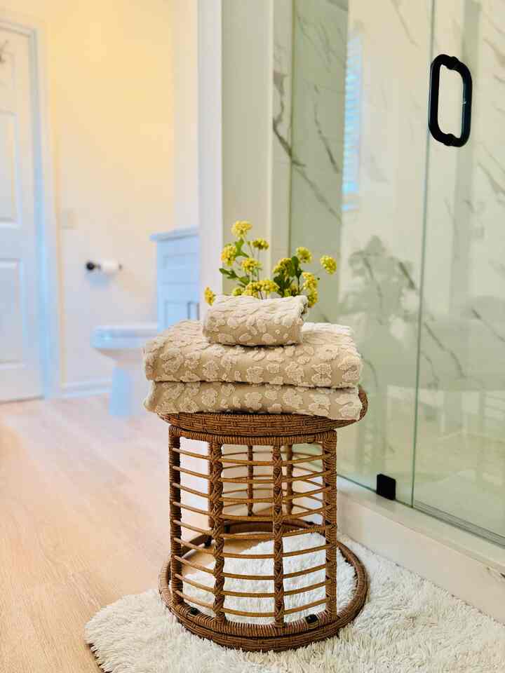 Natural wood-tone bathroom with wicker stool holding towels and a vase of flowers, creating a clean, warm atmosphere