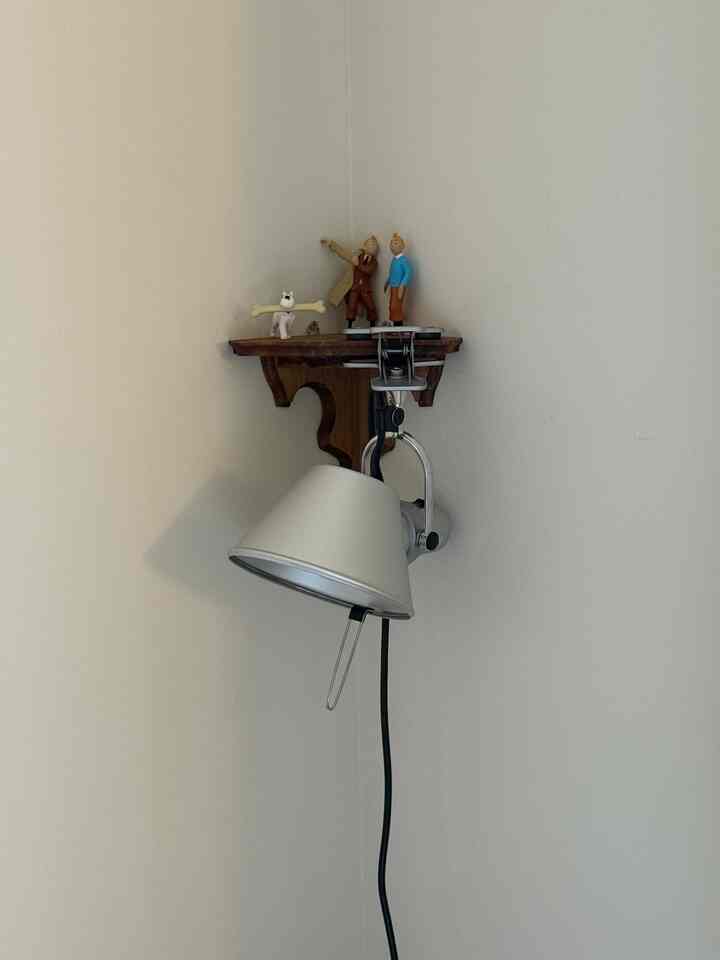 Cozy corner space with small wooden corner shelf mounted on white wall, silver clip-on lamp, and decorative figurines