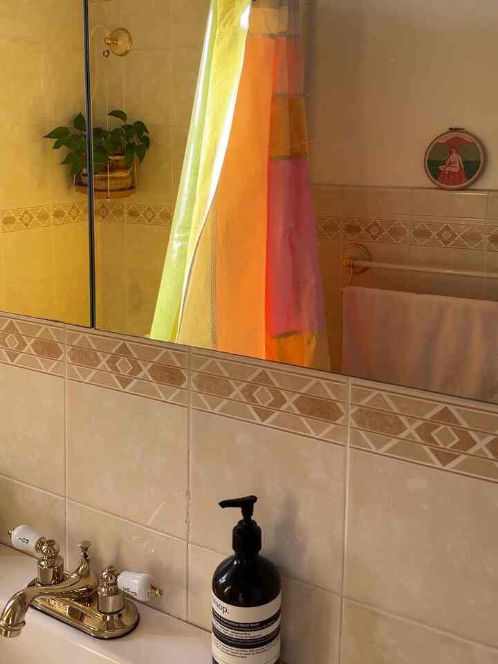 Warm beige and white bathroom featuring colorful curtain and gold faucet, creating a cozy atmosphere