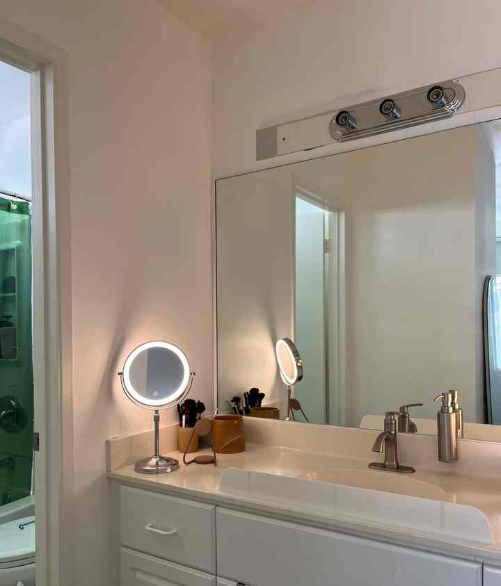 Bright white-toned bathroom powder room featuring lighted makeup mirror and gold ceramic pots in a compact makeup corner
