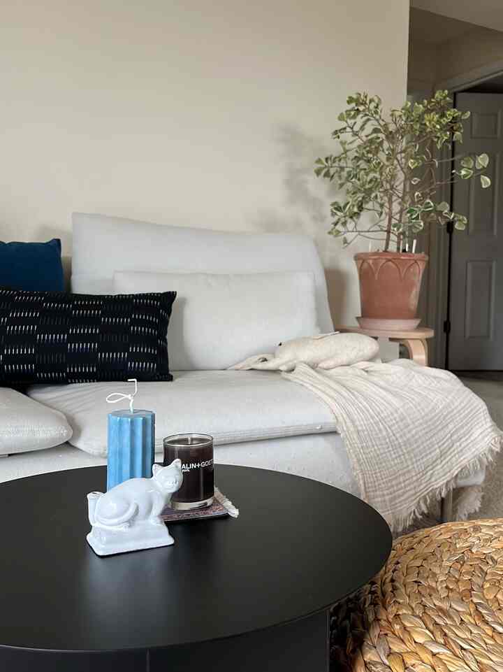 White-toned living room featuring sofa, side table with plant and candles, creating a cozy atmosphere