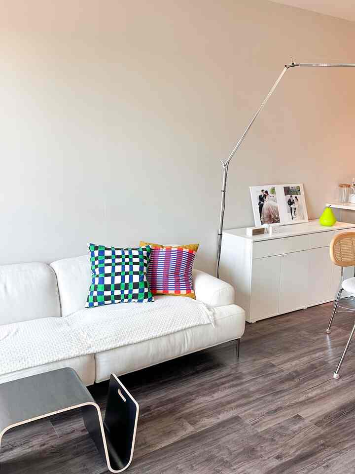 Modern white-toned living room featuring a white sofa, storage cabinet, and metal floor lamp with a clean atmosphere