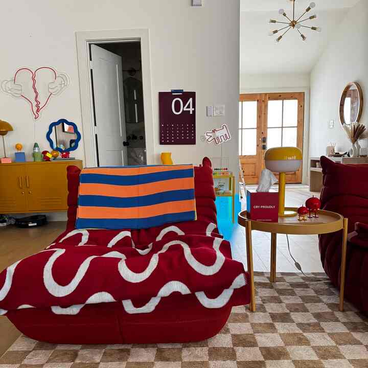 Bright living room with red togo armchairs featuring a blue-striped orange throw, yellow lamp, and side table