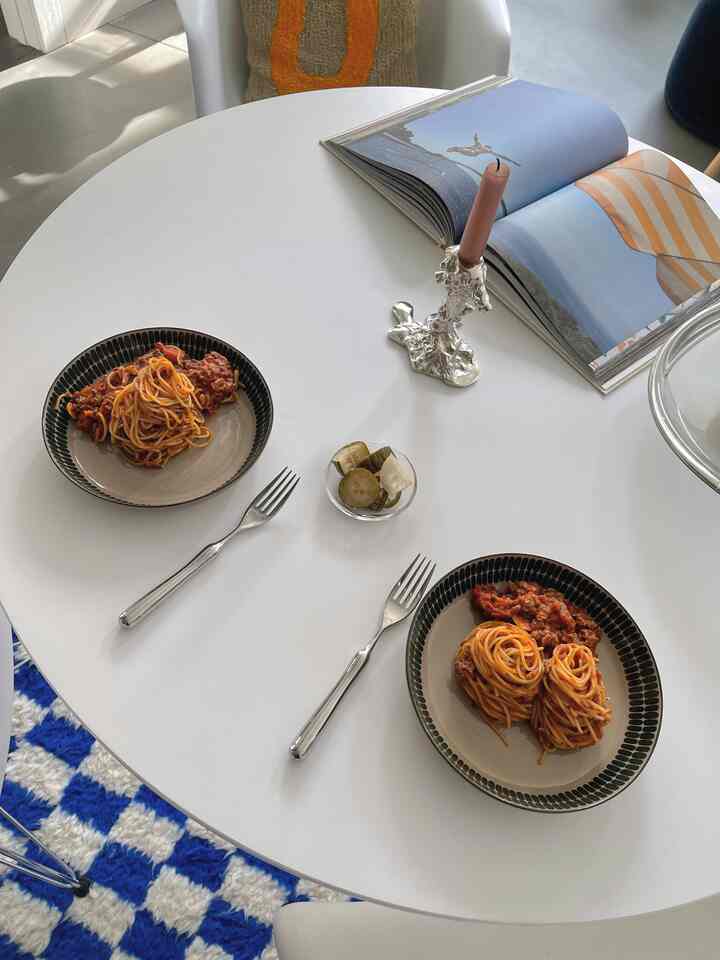 Clean home cafe scene with silver cutlery and pasta plates on a white round dining table alongside a silver candle holder