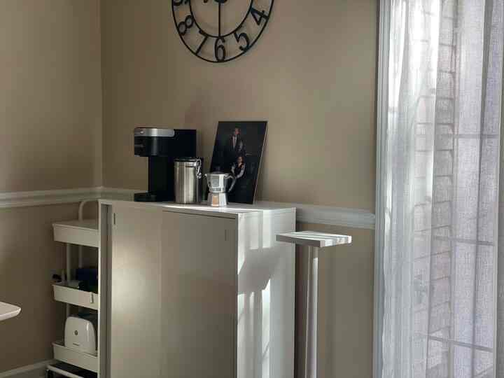 Beige walls and white furniture with sheer curtains near kitchen area featuring coffee equipment, creating a cozy home cafe vibe