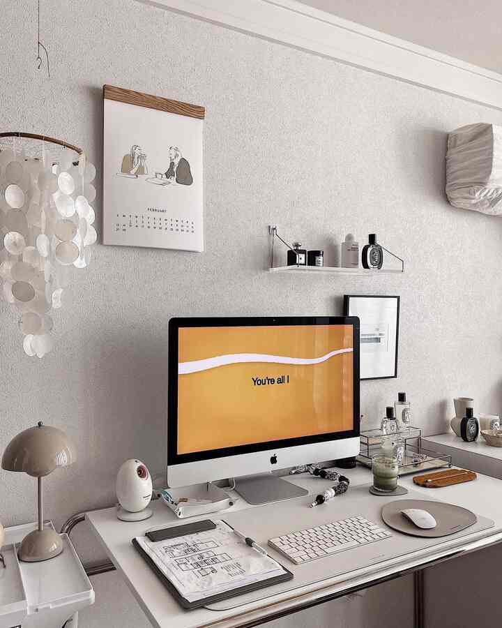 White-toned simple and modern home office space featuring a desk with iMac, calendar, and small desk accessories