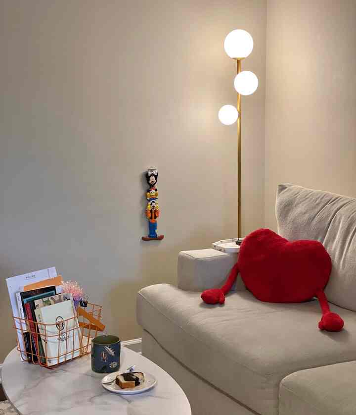 Beige sofa and marble table in a simple living room featuring a bright red heart-shaped cushion creating a cozy atmosphere