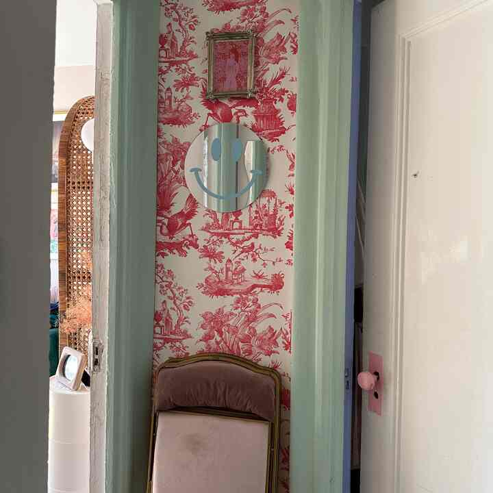 Red and ivory toned entrance space featuring vintage velvet folding chair and smiling face mirror with a colorful eclectic vibe