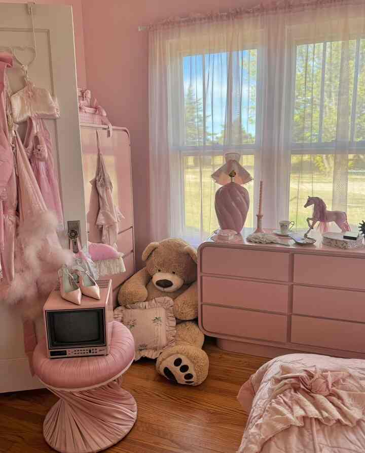 Pink-toned kids' room featuring vintage ottoman, table lamp, and a large teddy bear in a cozy bedroom setup