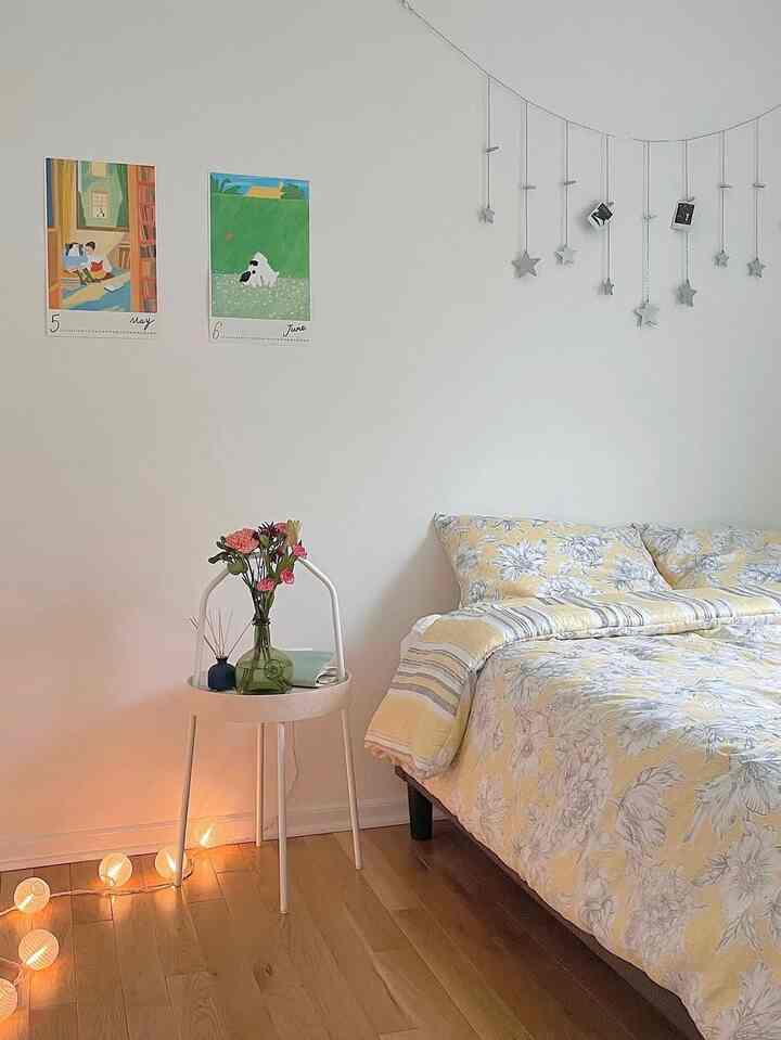 Bedroom with white walls and wood tone floor, featuring yellow floral bedding and a white side table creating a cozy atmosphere