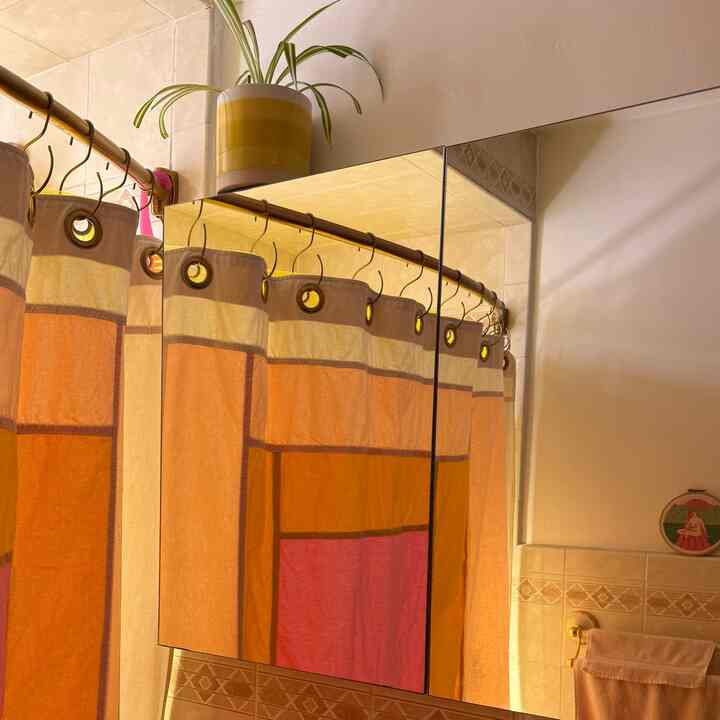 Warm-toned bathroom featuring orange and pink shower curtain with a reflective mirror cabinet