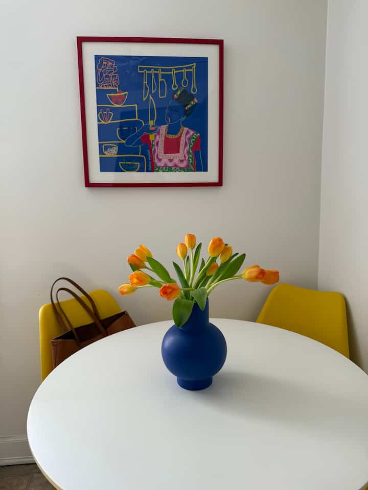 Bright dining space with white walls and round table, featuring yellow chairs and blue vase as modern vibrant accents