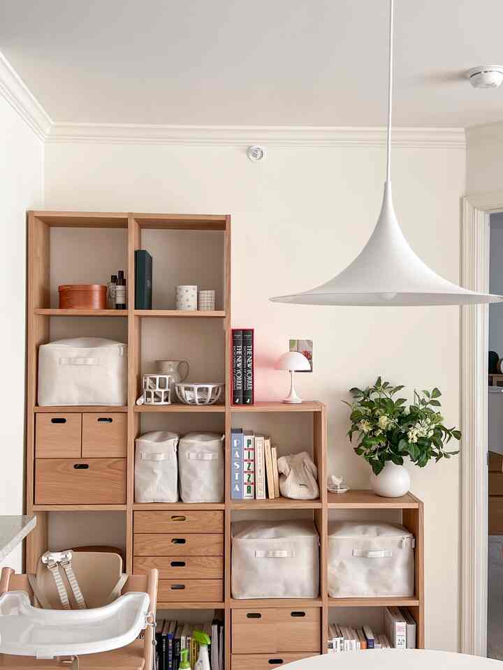 Natural-toned dining room featuring wood-tone bookshelf and white storage boxes, arranged simply and neatly with a pendant light