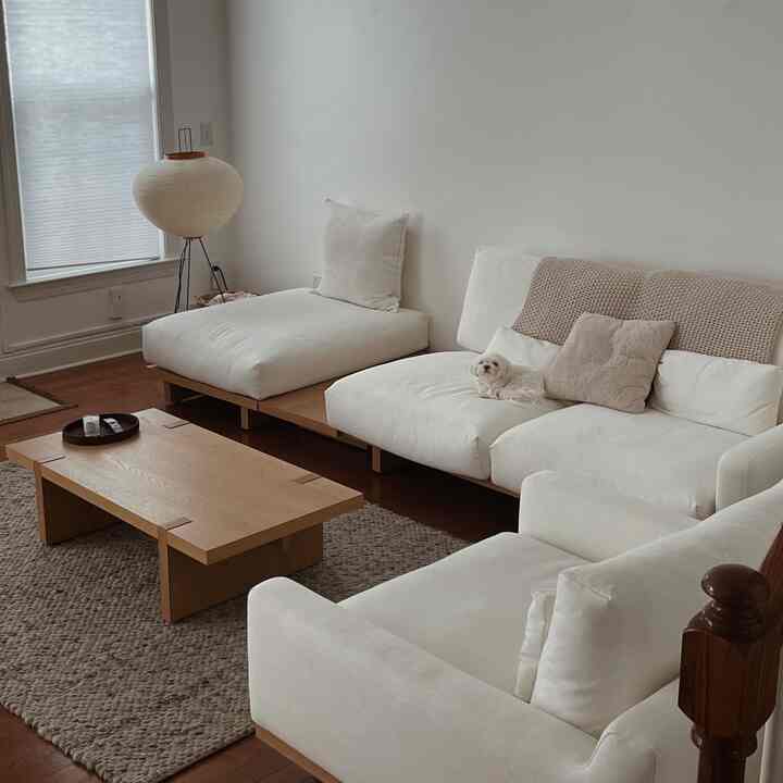 Modern living room in white and natural wood tones featuring minimalist sofas and a chunky knit rug with a clean atmosphere