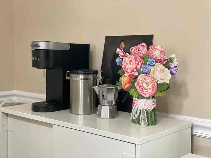 Beige wall and white shoe cabinet topped with a coffee machine, stainless canister, moka pot, and colorful flower vase in a cozy home cafe setup