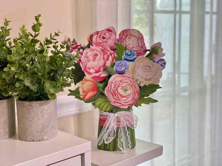 Natural toned dining room with pink flower card and green plant arranged on white furniture