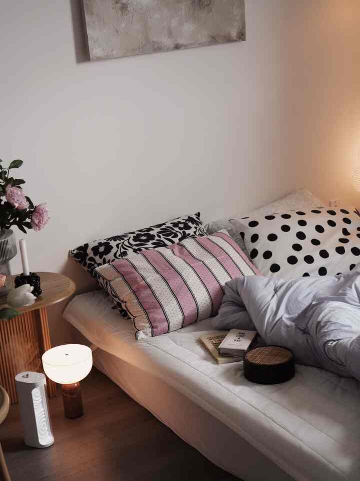 Natural color tone small bedroom featuring bed with cushions and a table lamp creating cozy atmosphere