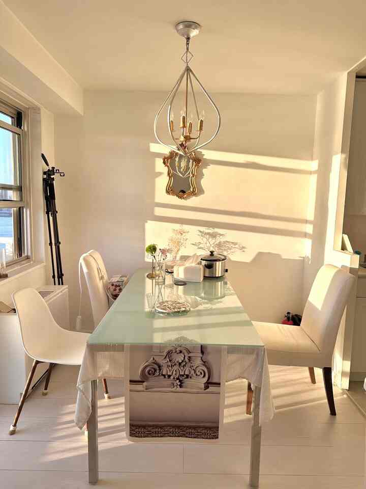 White and gold toned dining room featuring a transparent glass dining table and elegant chandelier lit by warm morning sunlight