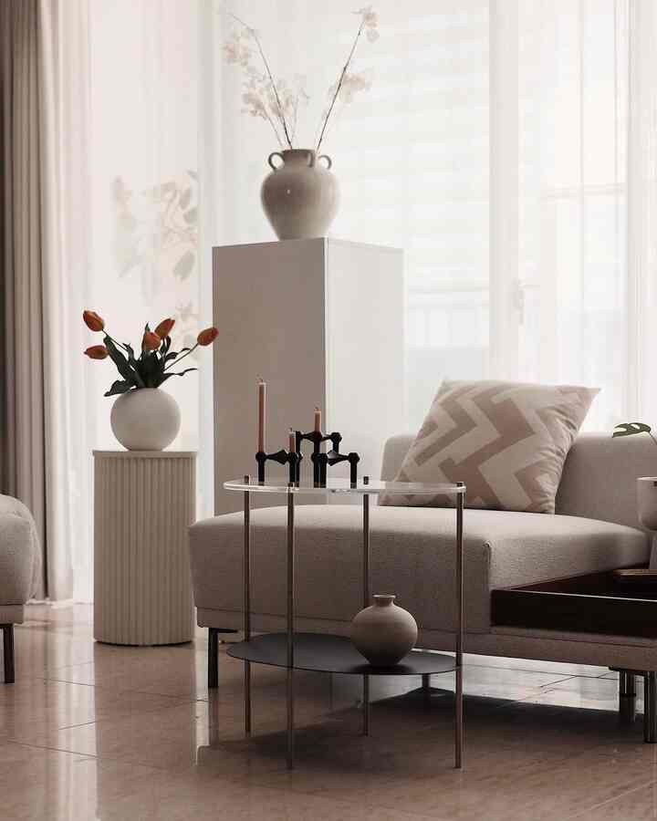 Beige and natural tone living room featuring sofa, cushions, candle holders on side table, and decorative vases creating a cozy atmosphere