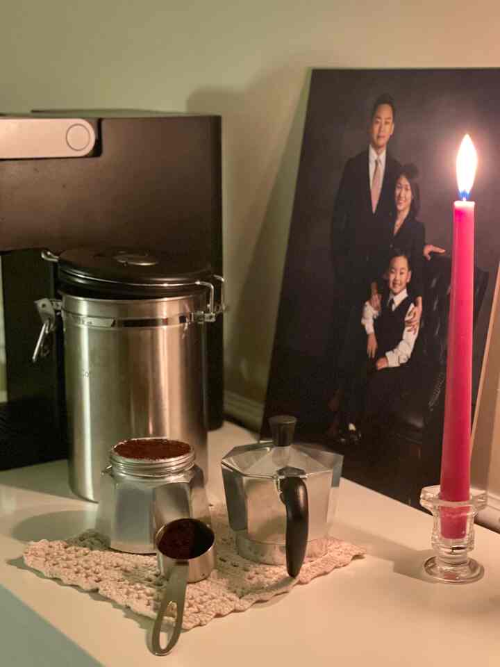 Cozy kitchen scene featuring a red lit candle and coffee equipment on a white surface with warm ambient lighting