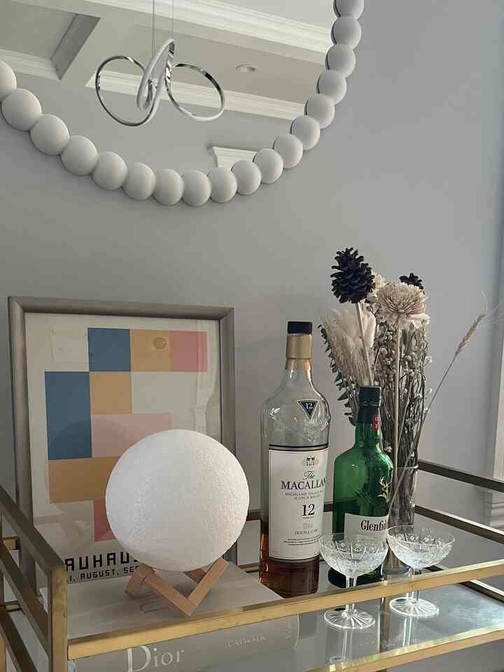 Silver metal frame bar cart featuring a spherical moon lamp, whiskey bottles, crystal glasses, and dried flowers in a cozy living room setting