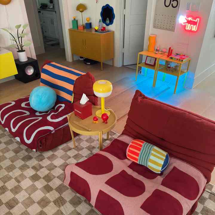 A cozy living room in red and yellow tones featuring armchairs with throws and a side table, accented by colorful decor elements.