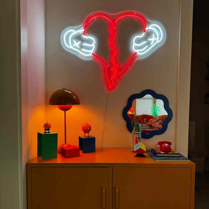 Colorful interior with mustard storage cabinet topped by retro accessories and a neon broken heart light