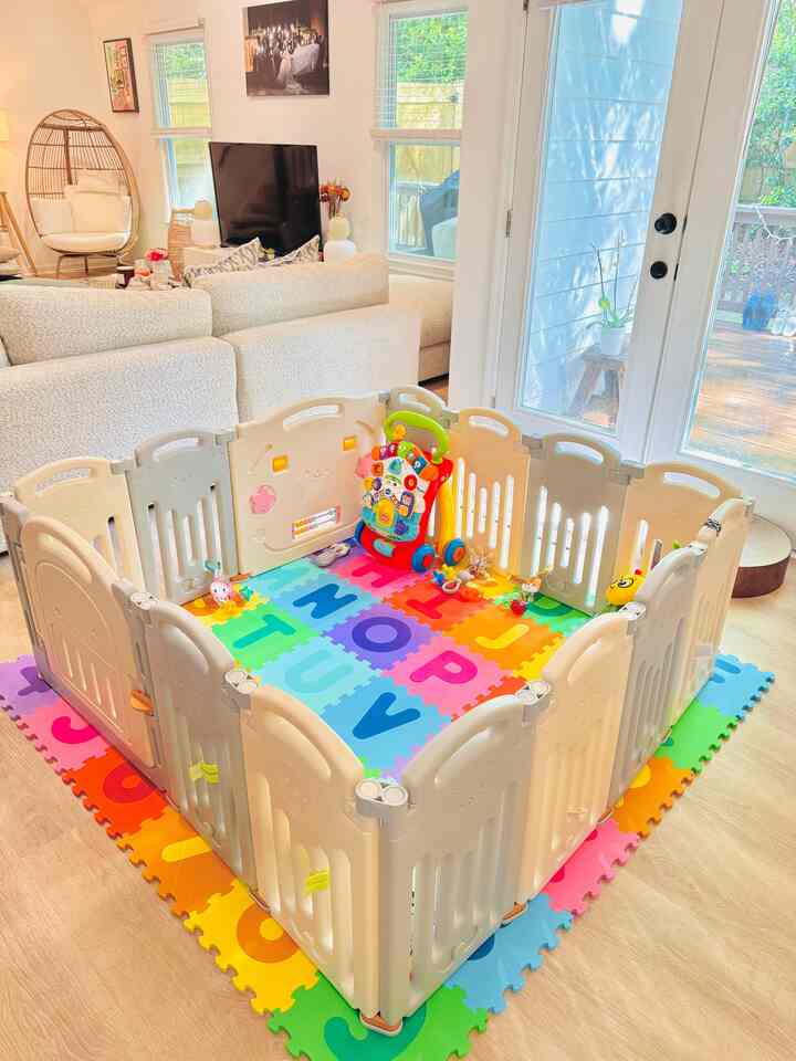 A beige and natural color living room featuring a baby safety fence and colorful alphabet play mats, creating a warm and inviting space